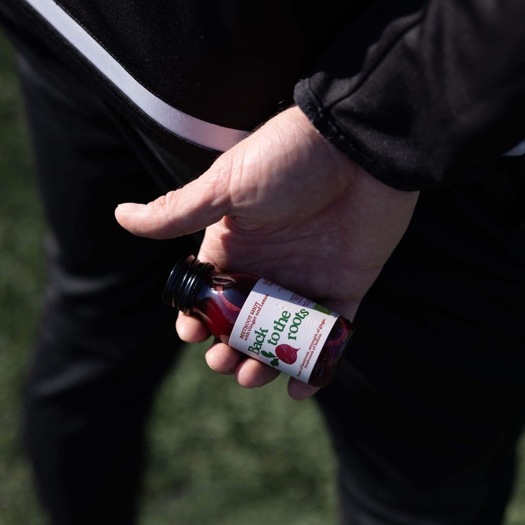 Sportowiec trzymający shot z buraka Back2TheRoots przy boisku